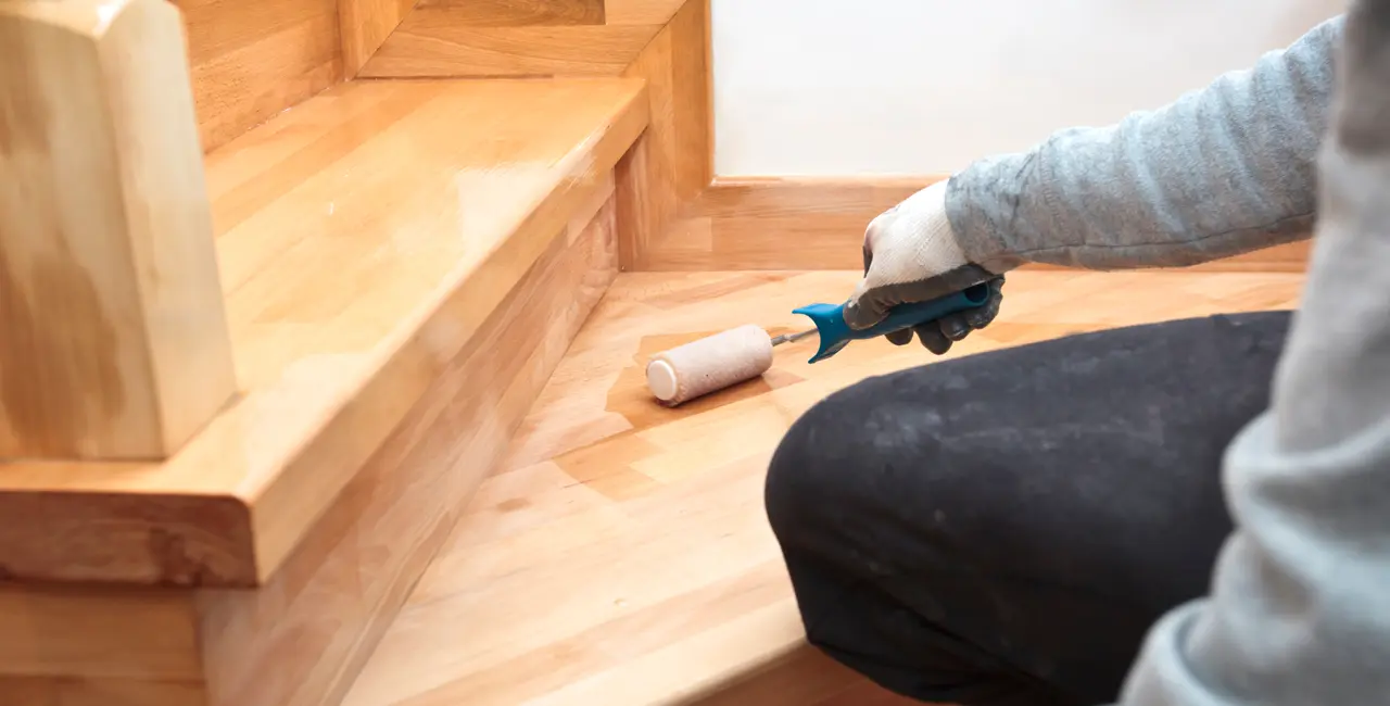 Cuidado de la madera, persona barnizando escalera de madera con un rodillo